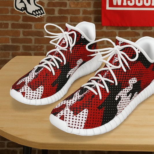 Red, black, and white patterned sneakers on a wooden table with a brick wall background.